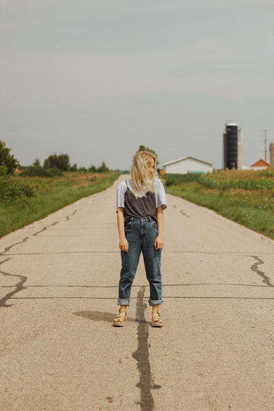 一个穿着白色t恤和蓝色牛仔牛仔裤的女人白天走在灰色的水泥路上